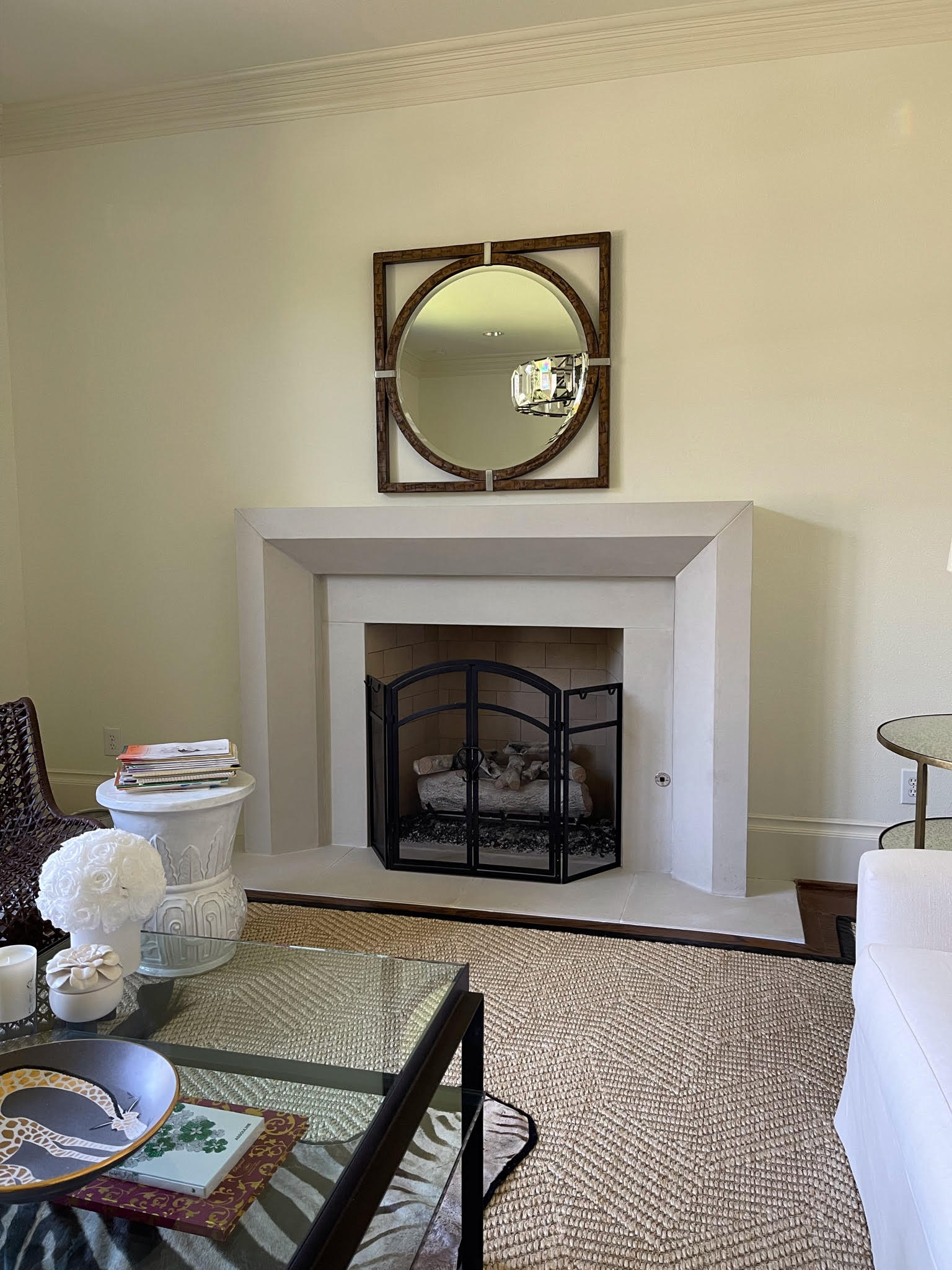 Cream cast stone mantel with round mirror and black fireplace doors